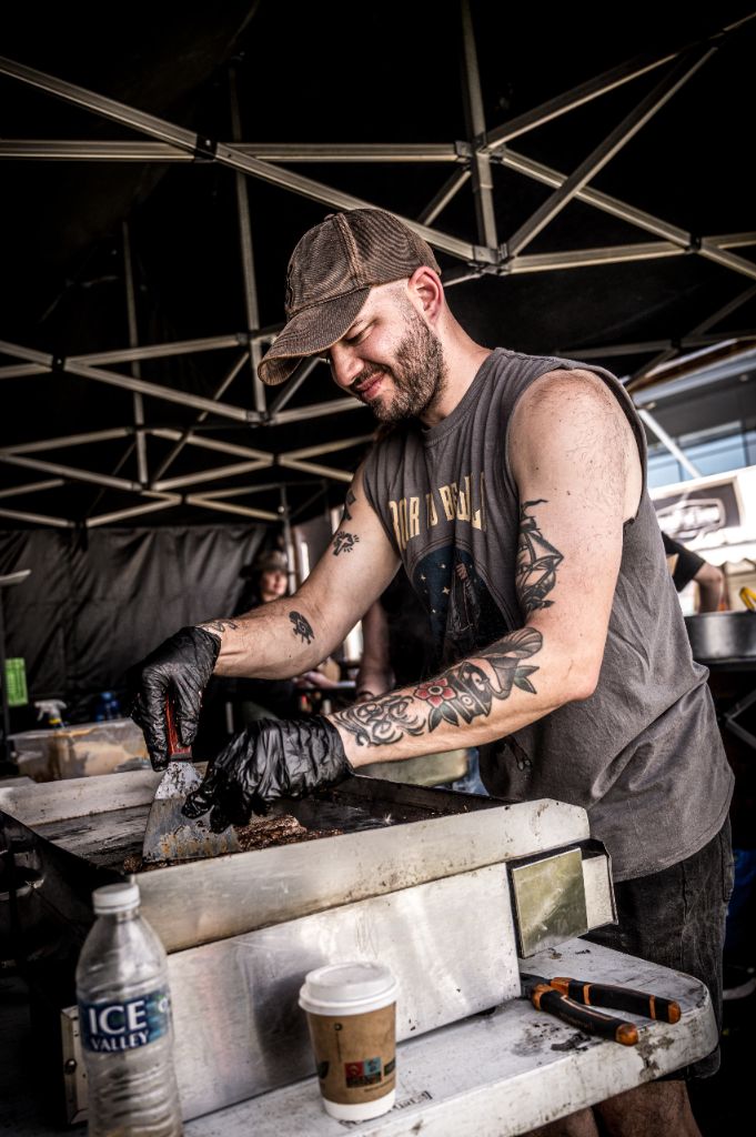 Chef working the plancha at a festival, tattooed arms with spatula