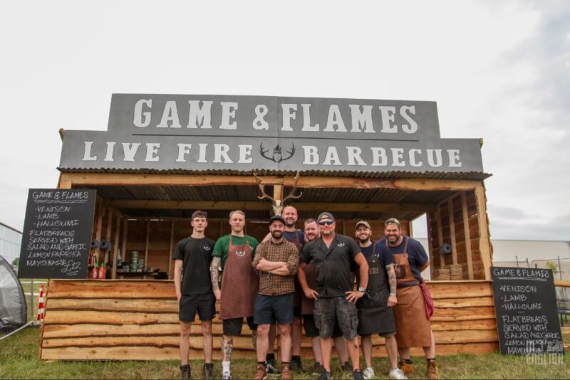 The Game and Flames live fire barbecue stand fully set up with equipment, menus and team at a festival