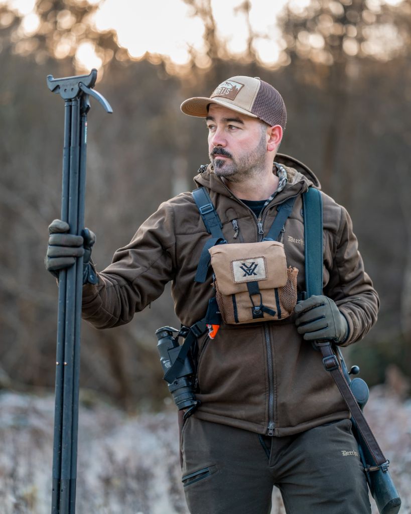 Cai Ap Bryn holding shooting sticks with rifle slung, portrait in winter woodland