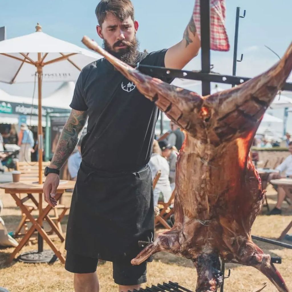 Cai preparing a whole deer on a spit at a festival