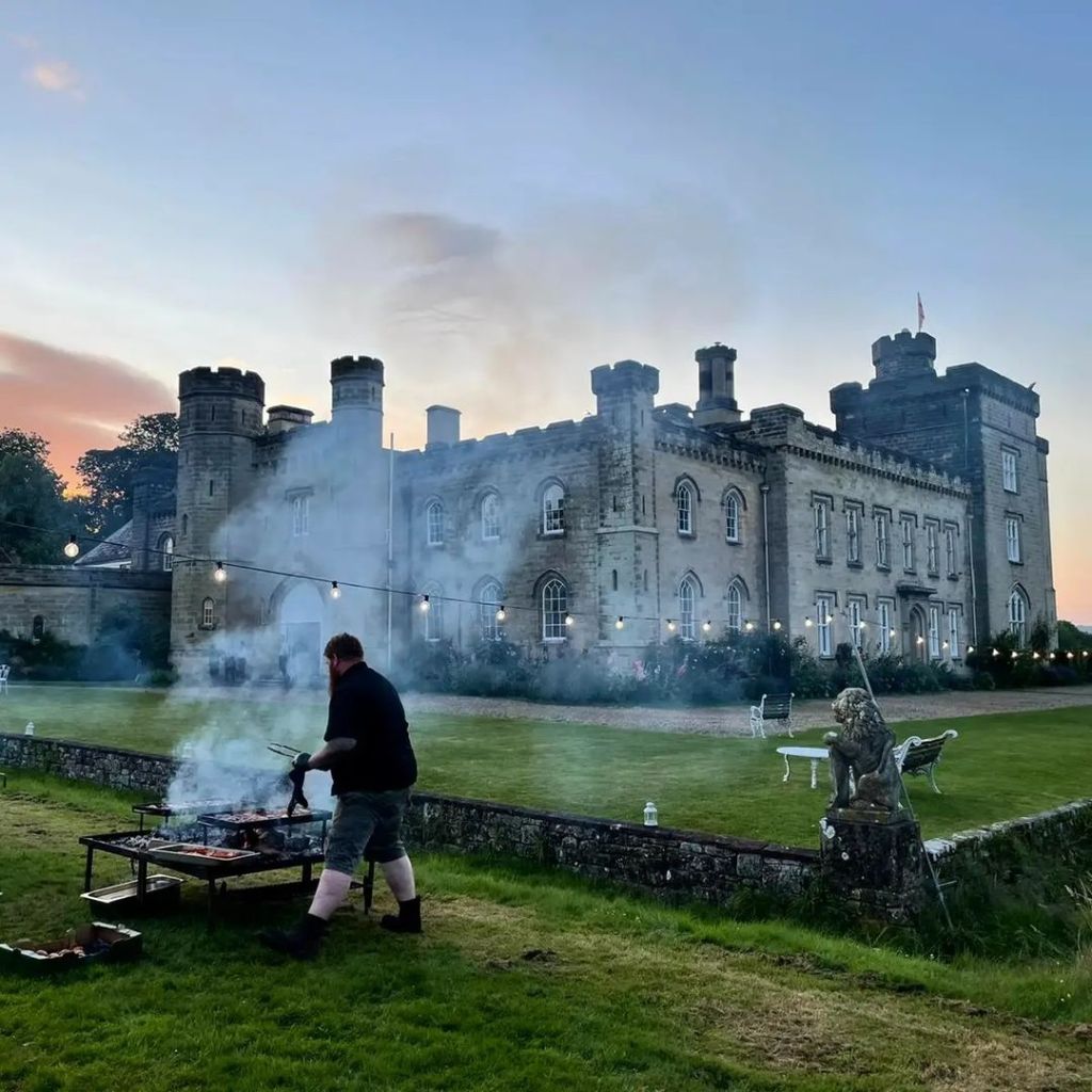 Game and Flames live fire setup at a castle wedding venue at sunset with festoon lights