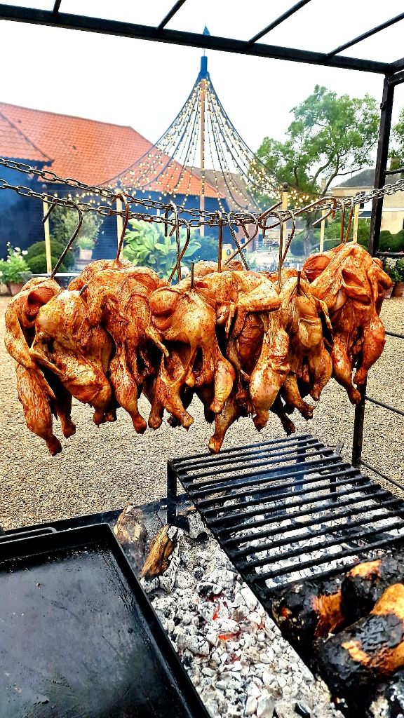 Whole chickens hanging on chains over live fire at a wedding venue