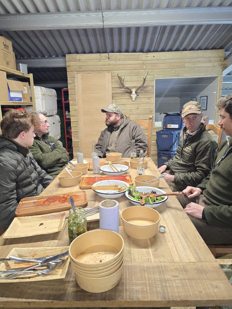 Workshop group enjoying a communal meal around a wooden table with antler mount